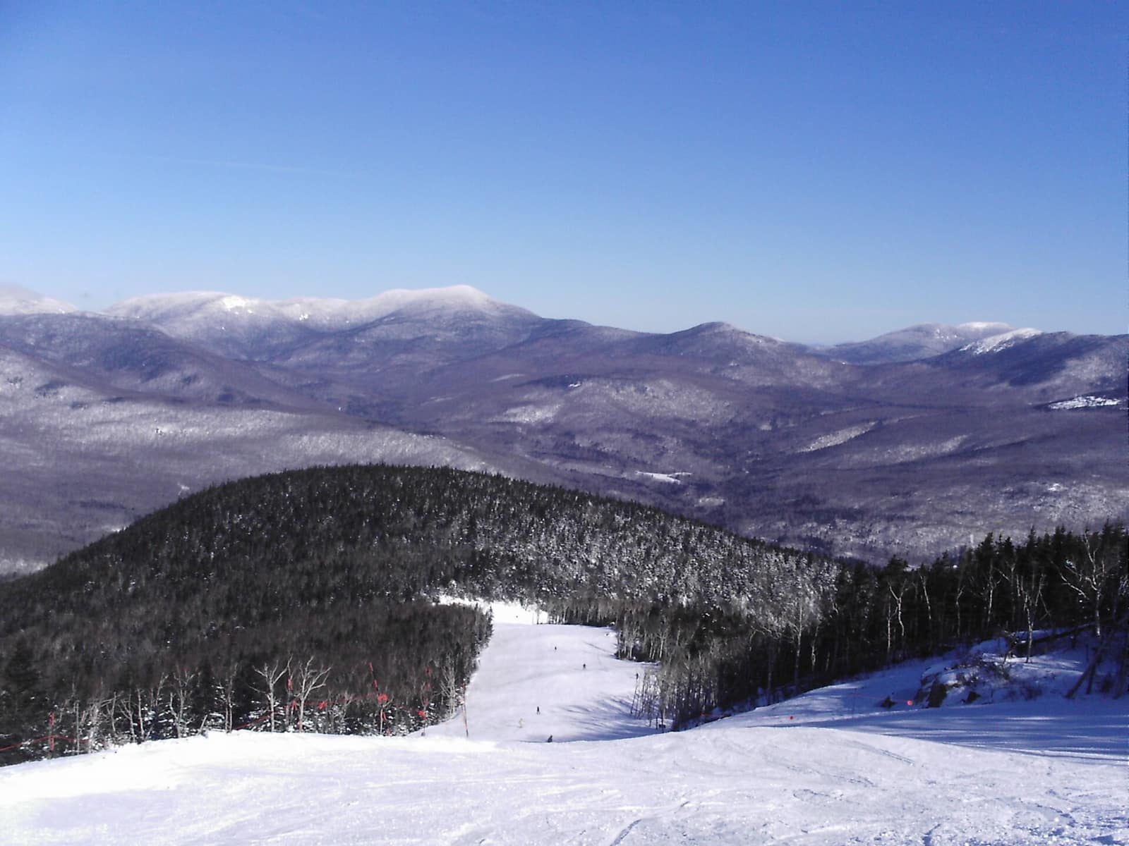 Wide view from the upper slopes of Sunday River ski resort looking out over the snow-covered western Maine mountains