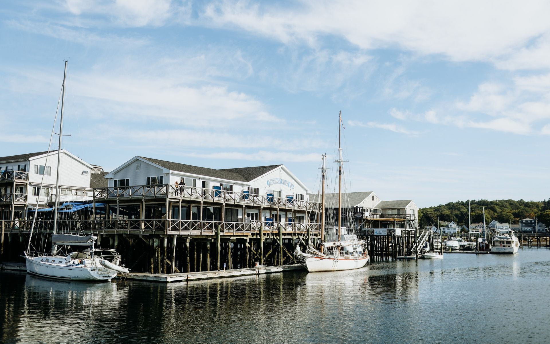 Bar Harbor village waterfront with wooden pier, lobster boats in Frenchman Bay, and the forested slopes of Mount Desert Island in the background