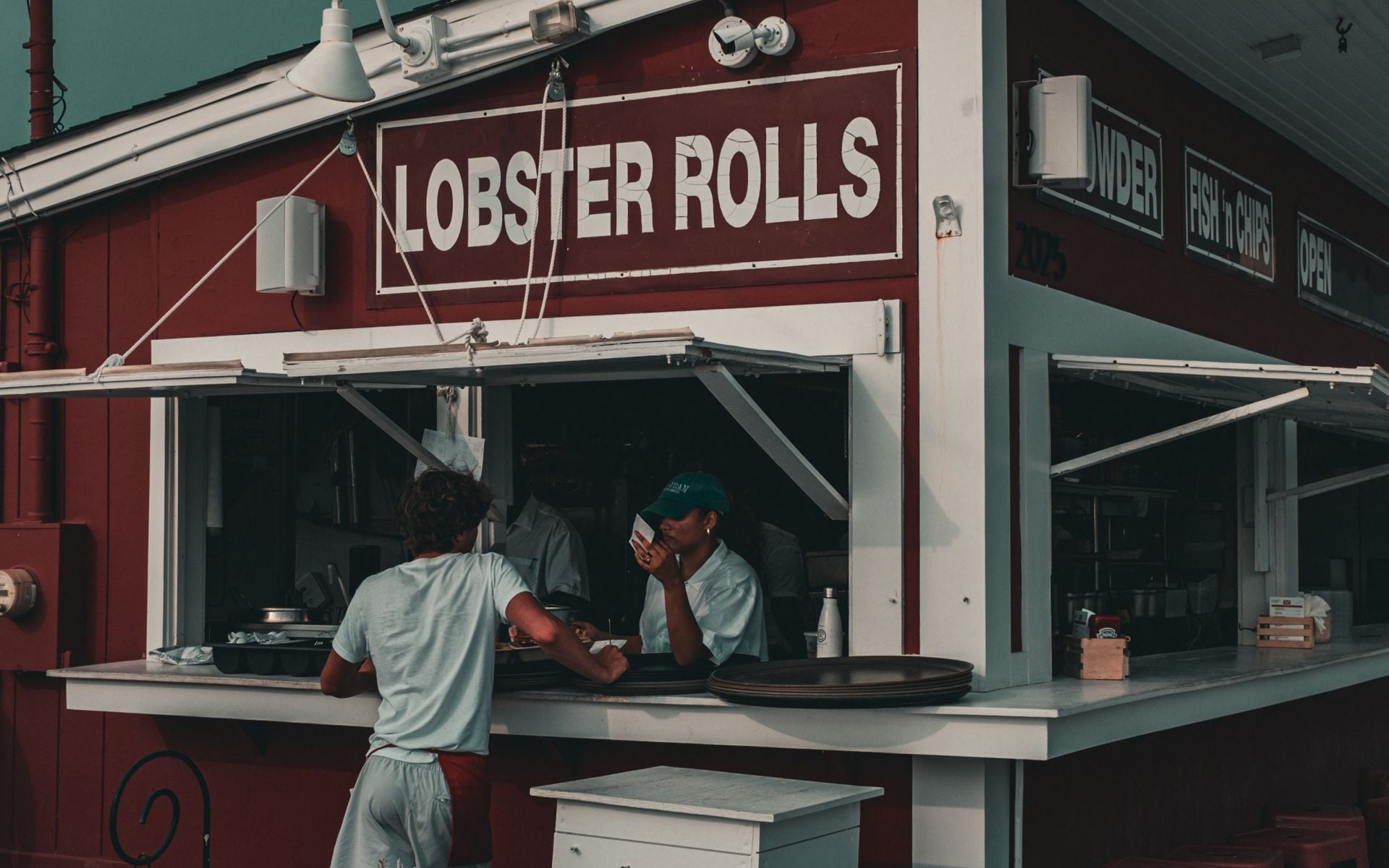 A red lobster roll on a toasted split-top bun at a Maine waterfront lobster shack with harbor in the background